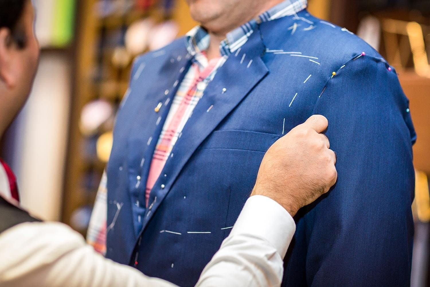 Tailor fitting a blue suit jacket on a customer.